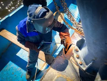 Welder working on boat hull with chains overhead