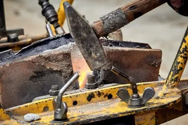 Welding repair on heavy equipment yellow machinery with hammer and flame