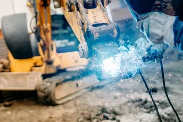 Welder welding excavator bucket attachment with bright arc sparks